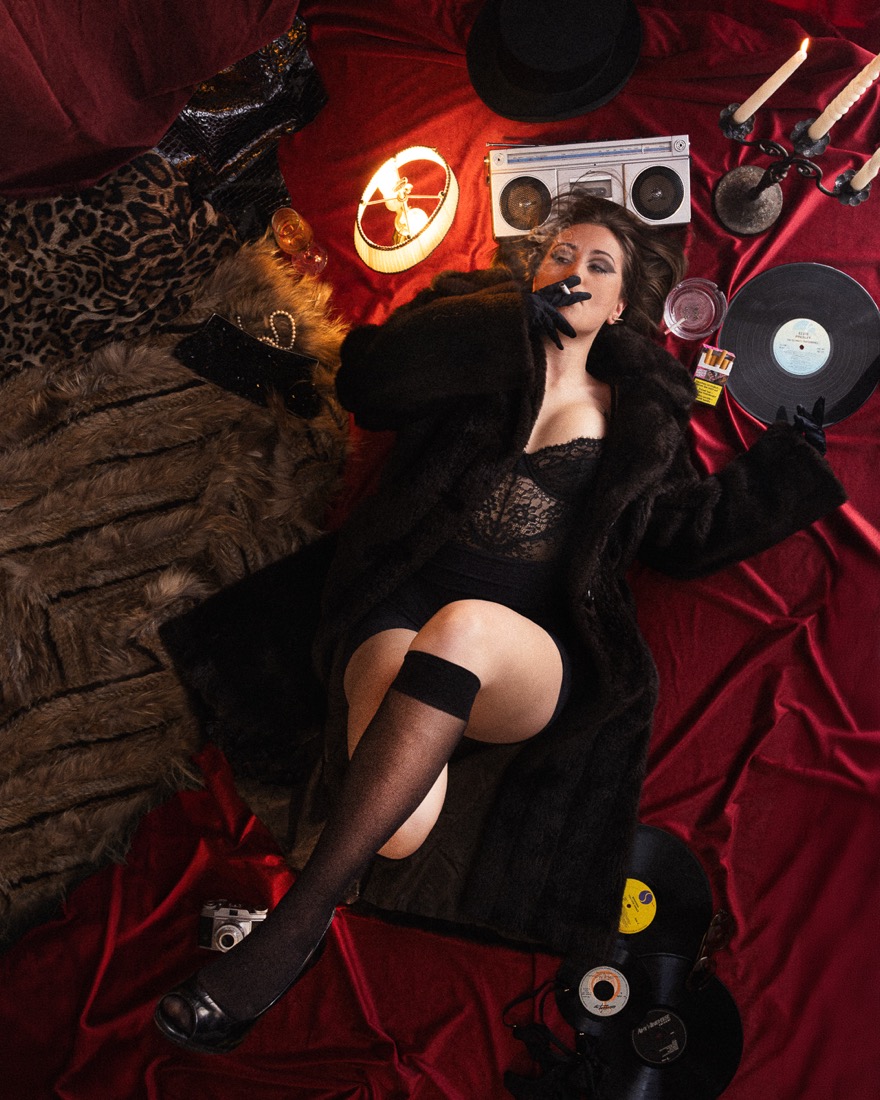 Pose allongée en corset et manteau de fourrure, entourée de vinyles et de bougies