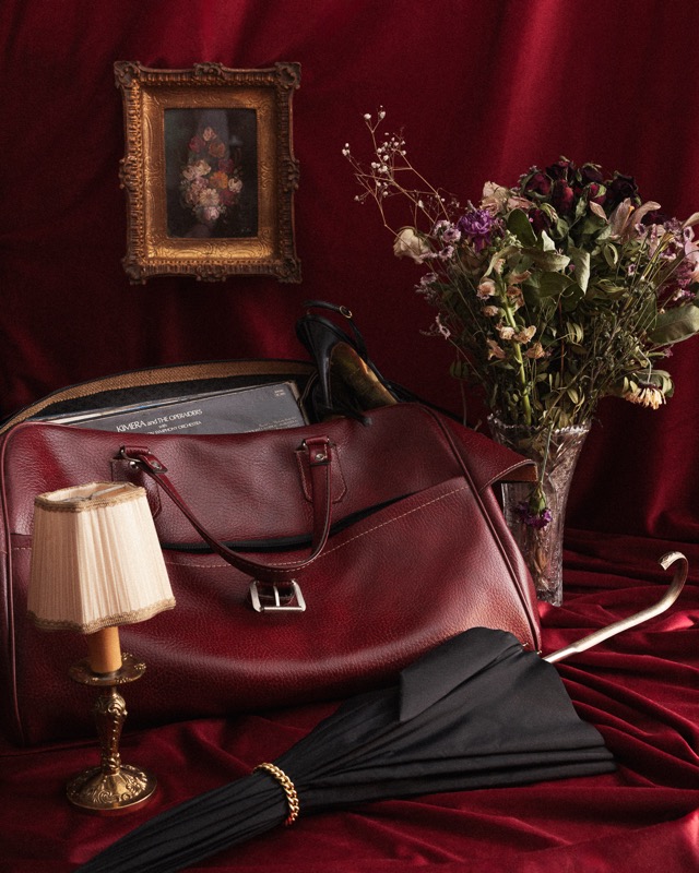 Sac de voyage bordeaux, lampe, bouquet séché et parapluie sur velours rouge